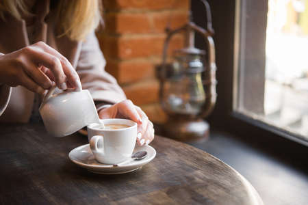 woman in a cafe pours milk cream into coffee cup. businesswoman  lifestyle backgroundの写真素材