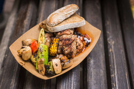 street grill bbq set of meat and vegetables, mushrooms and zucchini in a paper plate on the bench. Delicious snack at the street food festivalの写真素材