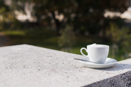 White coffee cup with foam on a street at green park, sunny dayの写真素材