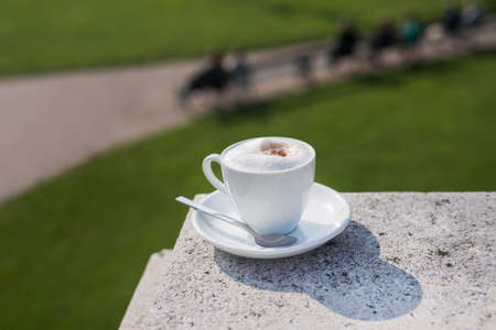 White coffee mug with foam on a street at green park, sunny dayの写真素材