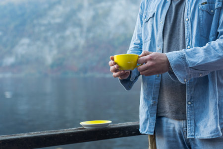 Man with a yellow cup of coffee, morning by the river on the pier with hot drinkの写真素材