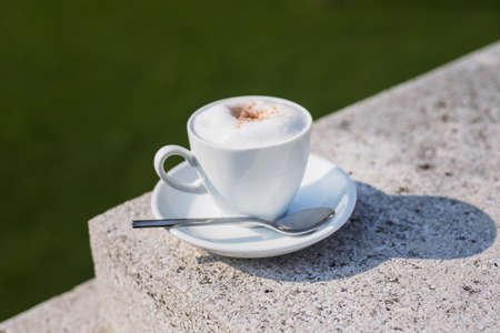 White coffee cup with foam on a street at green park, sunny dayの写真素材