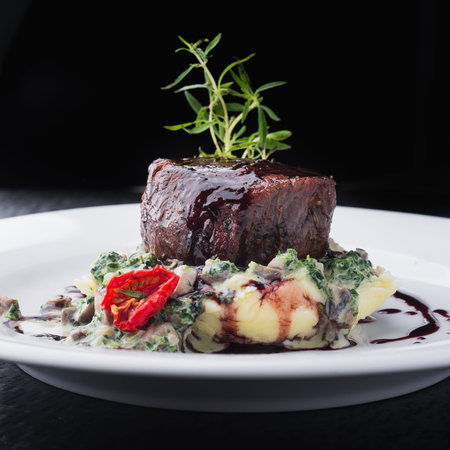 steak medallion with tomatoes and sauce on a white plate. restaurant food. black backgroundの写真素材