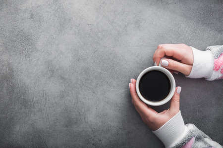woman in warm sweater holds a white cup of coffee on gray stone table. concept of warming up the drink in coldの写真素材