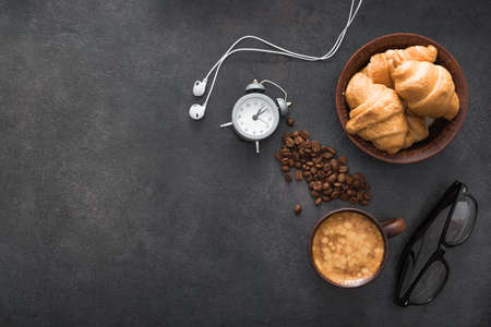 coffee cup with croissant and alarm clock, black glasses, white headphones. light snack during work. concept of business lunch. top viewの写真素材