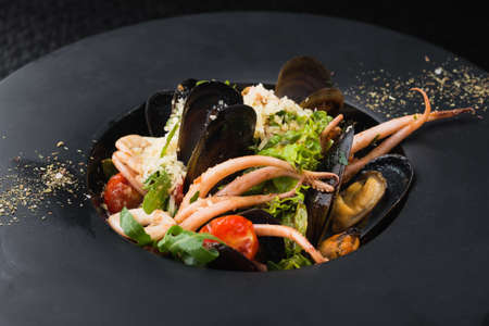 seafood, squid and mussels in a black plate. dish at the restaurantの写真素材