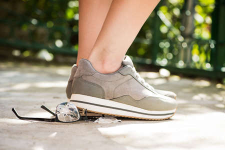 woman at the walk stepped on the glasses. unfortunate incident on the street. broken eyeglasses on asphaltの写真素材