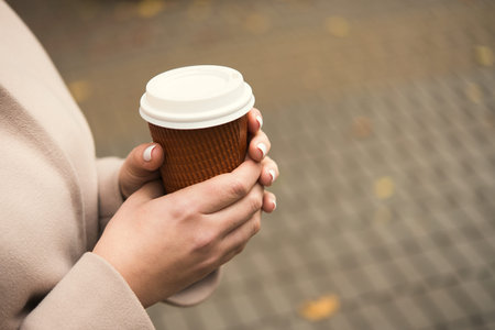 Woman drinking take away coffee cup, walk in the autumn weather in the park