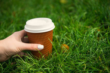 morning fresh coffee concept with paper cup on green grass and woman hand on backgroundの写真素材
