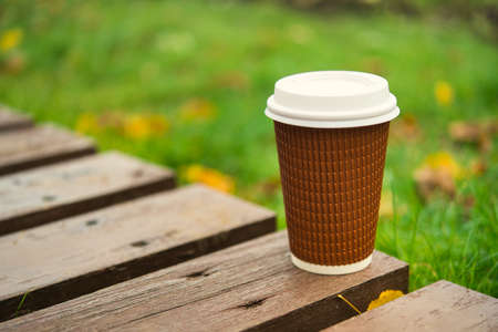 Paper cup take away coffee on a wooden bench in the park, cold autumn weather の写真素材
