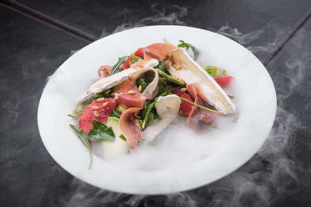 fresh salad with prosciutto and brie cheese, grapefruit and cashew nuts in a white plateの写真素材