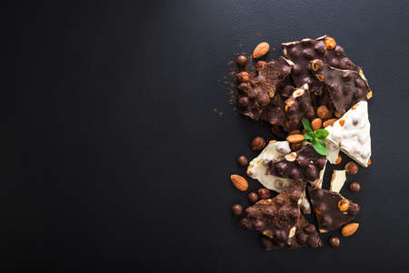 pieces of black and white chocolate with nuts, fresh mint and almond on black background, top viewの写真素材