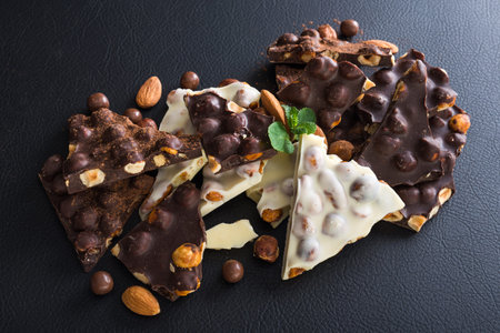 pieces of black and white chocolate with nuts, fresh mint and almond on black background