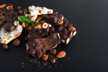 pieces of black and white chocolate with nuts, fresh mint and almond on black background