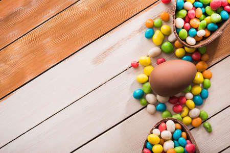easter dessert tasty chocolate egg with color candy dragee on wooden tableの写真素材