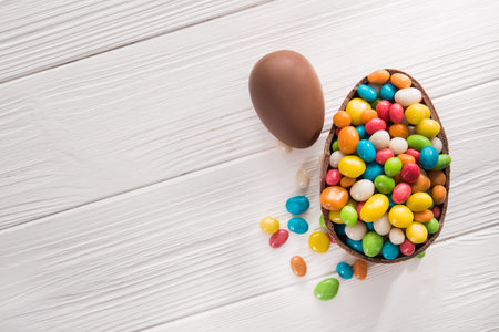 easter dessert tasty chocolate egg with color candy dragee on wooden table. top view
