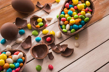 easter dessert tasty chocolate egg with color candy dragee on wooden tableの写真素材