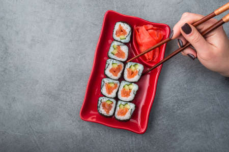 woman holding sushi roll in chopstick, on stone backgroundの写真素材