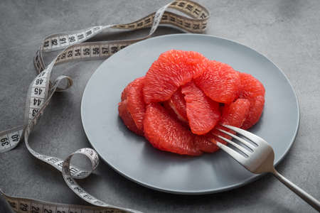 Fresh sliced grapefruit on a plate with white measuring tape, stone table. Concept of diet.の写真素材