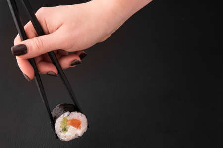 woman hand holding one sushi roll with cucumber and salmon on a black backgroundの写真素材