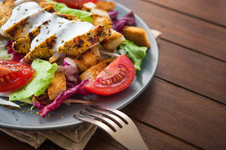 fresh salad with grilled chicken, tomato, cracker bread on wooden table. healthy colored foodの写真素材