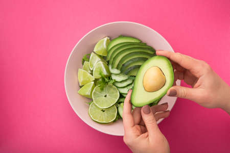 a woman holds a plate with a dietal avocado salad in her hands on pink table. Diet concept healthy food. top viewの写真素材
