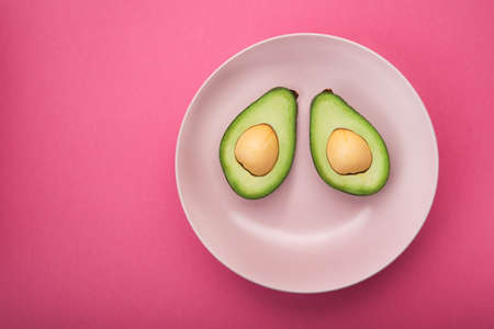 Green avocado on a plate, pink pastel background. Diet food. top view. Funny smileの写真素材