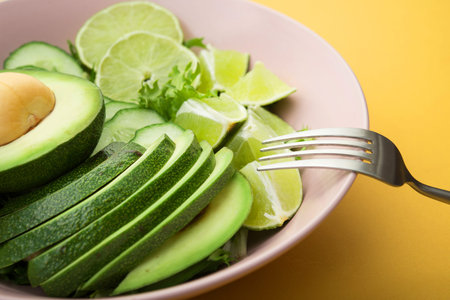 Fresh salad with avocado, green lime and cucumber on a pastel yellow background. Diet concept food