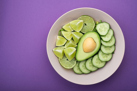 Salad with avocado, fresh lime and green cucumber on a violet background. healthy organic food....