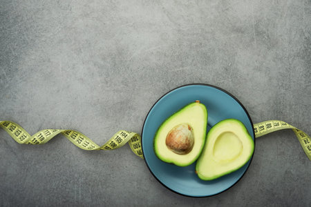Fresh green avocado on a plate, stone table, diet time with measuring tape. top view