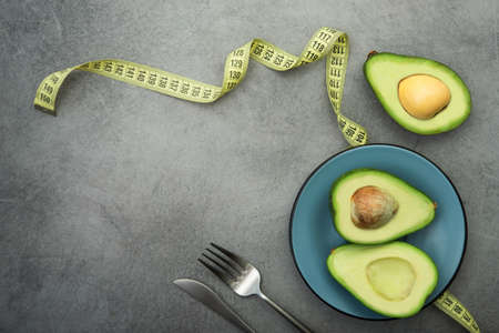 Fresh green avocado on a plate, stone table, diet time with measuring tape. top viewの写真素材