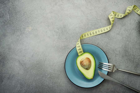 Fresh green avocado on a plate, stone table, diet time with measuring tape. top viewの写真素材