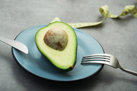 Fresh green avocado on a plate, stone table, diet time with measuring tape