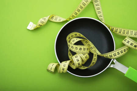 Yellow measuring tape in a empty pan, green color background. Diet concept. Top viewの写真素材