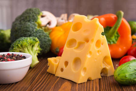piece of cheese with fresh vegetables on a table. Dairy product background.の写真素材