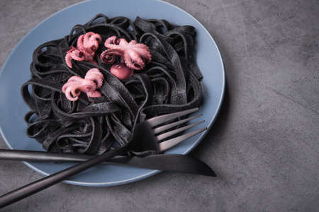 Italian black pasta with cuttlefish ink and marinated octopus on a plate, stone table. Tasty asian seafood.の写真素材