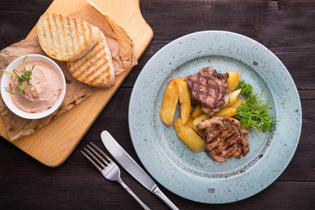 Tasty steak with potatoes on a blue plate on wood table. Grilled meal at lunch