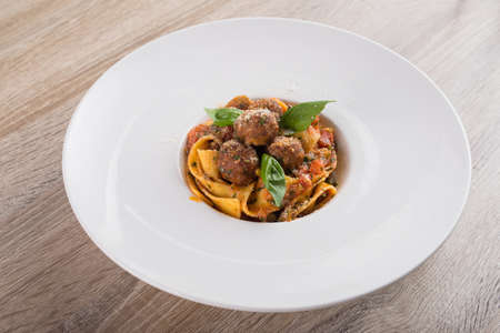Fresh pasta with meat balls in a white plate, wooden tableの写真素材