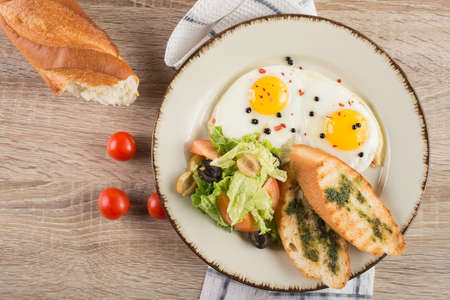 Fresh fried eggs with toast and vegetables on a wooden background. breakfast at the table in the restaurantの写真素材