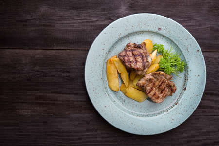 Tasty steak with potatoes on a blue plate on wood table. Grilled meal at lunchの写真素材