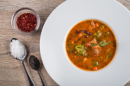 Tasty red goulash soup with tomato, beef and broccoli on a white plate. top viewの写真素材