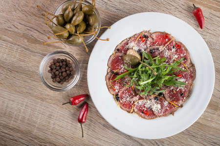 Beef carpaccio with arugula and capers on a wooden tableの写真素材