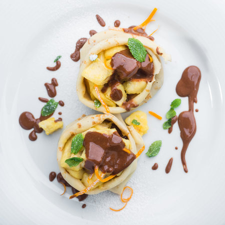 Delicious pancakes with bananas and pineapples are full of chocolate on a white plateの写真素材