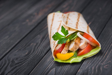 One tortilla wrap with grilled chicken and fresh vegetables on a wooden board. Mexican fast food background.の写真素材