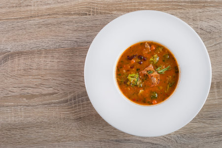 Tasty red goulash soup with tomato, beef and broccoli on a white plate. top viewの写真素材