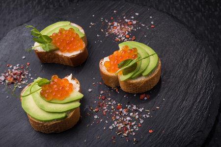Tasty bruschetta with avocado and caviar on a black slate board. appetizer snack background