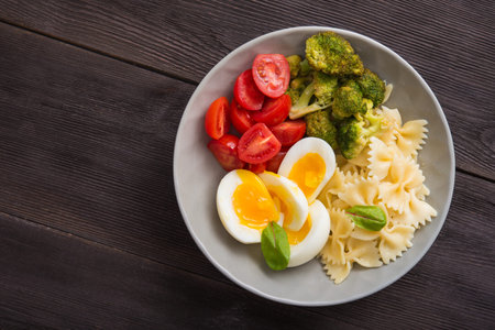 Farfalle pasta with egg, tomato and broccoli in a bowl. Healthy food diet background. Top view.