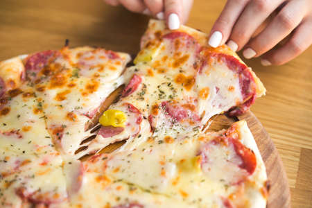 woman takes a hot piece of pizza with cheese, salami and pepperoni in italian cafeの写真素材