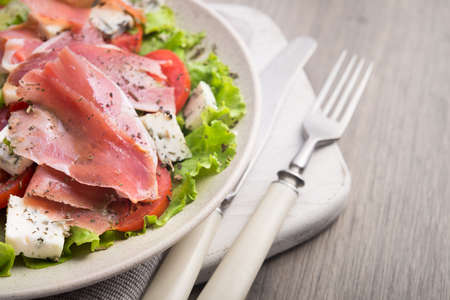 Fresh salad with prosciutto, tomato, lettuce and cheese blue on a stone wooden worktop, close upの写真素材