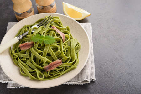 green spinach tagliatelle pasta with basil and anchovies in a plate on table. italian seafoodの写真素材